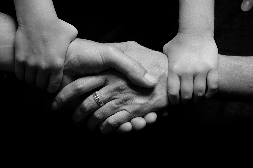 Image of hands, adults shaking hands with a child holding each adult's wrist, used to depict a parenting plan